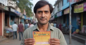 A man standing on a busy street holds up a “Dear Bumper Lottery” ticket toward the camera, with shops and pedestrians blurred in the background and the text “Lottery Sambad” displayed in the top-left corner.